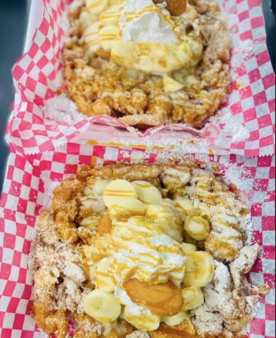 Two loaded funnel cakes in red-checkered baskets topped with banana slices, caramel drizzle and powdered sugar