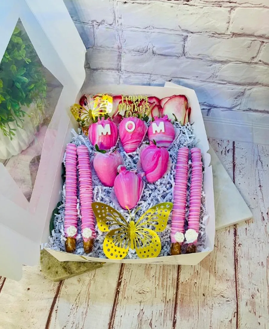 Pink-themed dipped treat gift box with chocolate-covered strawberries spelling MOM and a gold butterfly