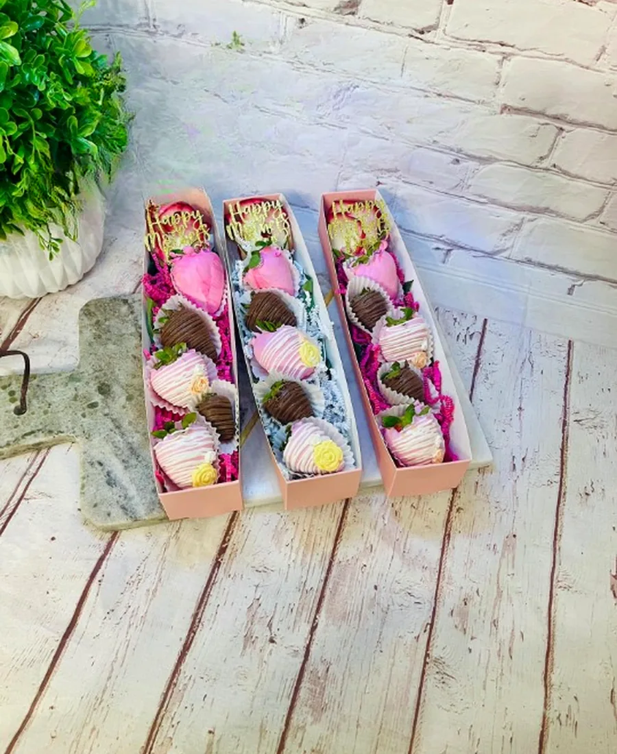 Three pink boxes of chocolate-covered strawberries lined up on a marble board